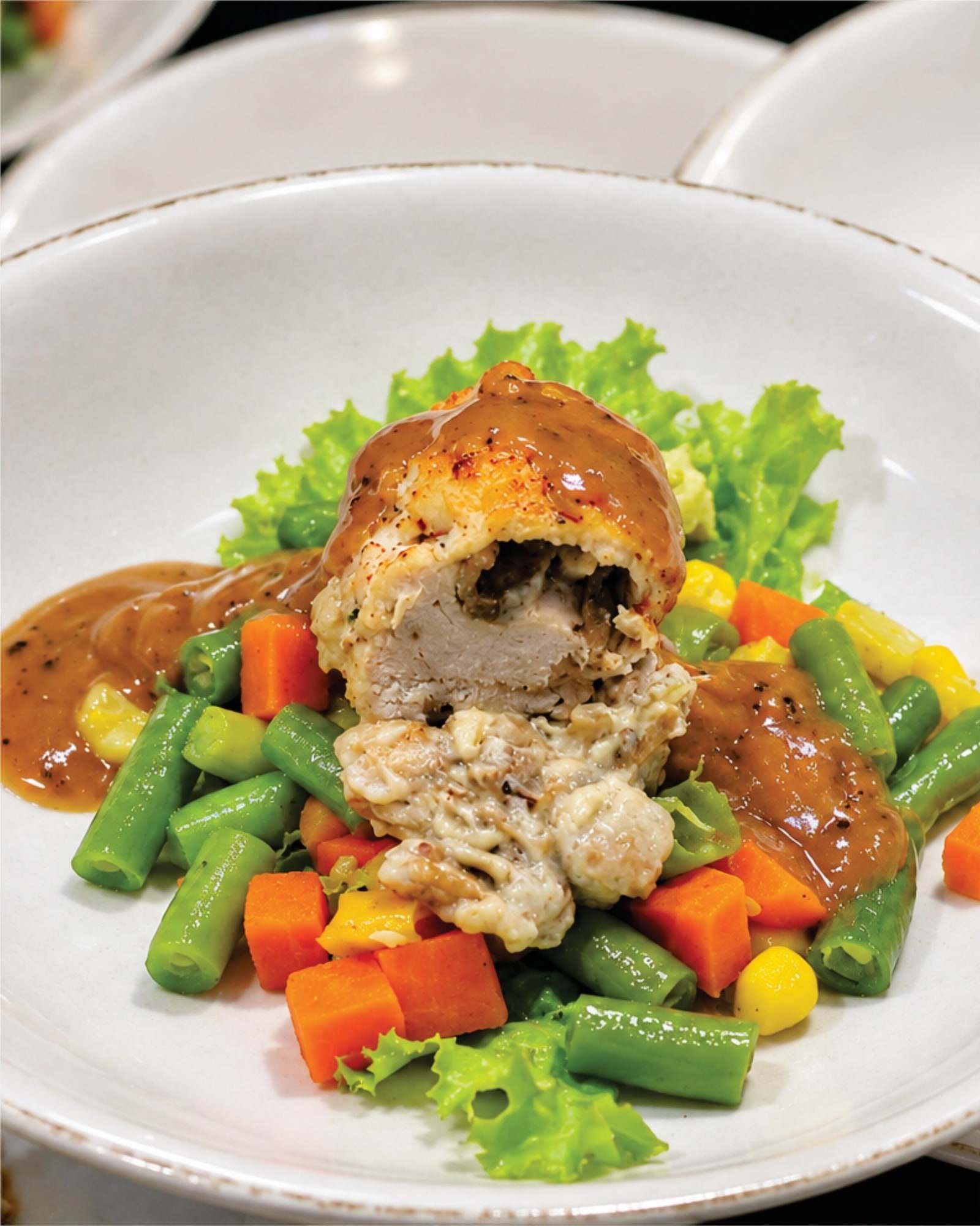 Chicken ballotine dengan saus cokelat, buncis, wortel, dan jagung di piring putih