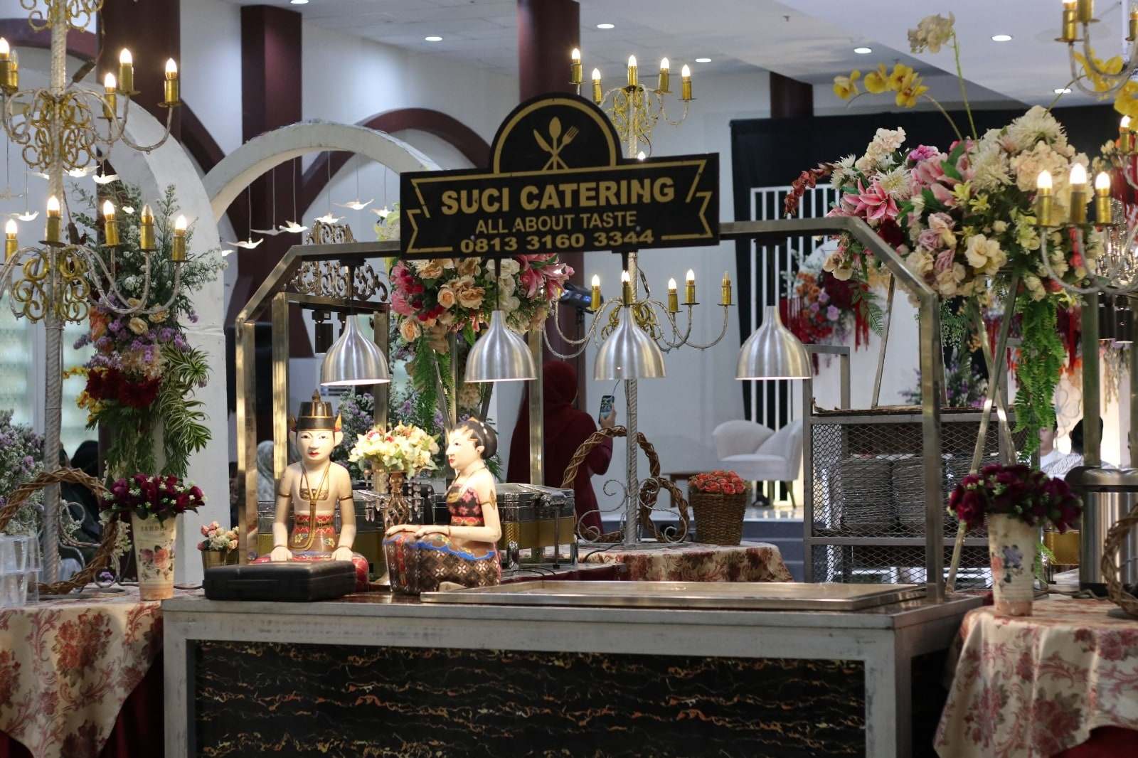 Gubukan Suci Catering berhias bunga dan lampu gantung dengan papan nama di atasnya