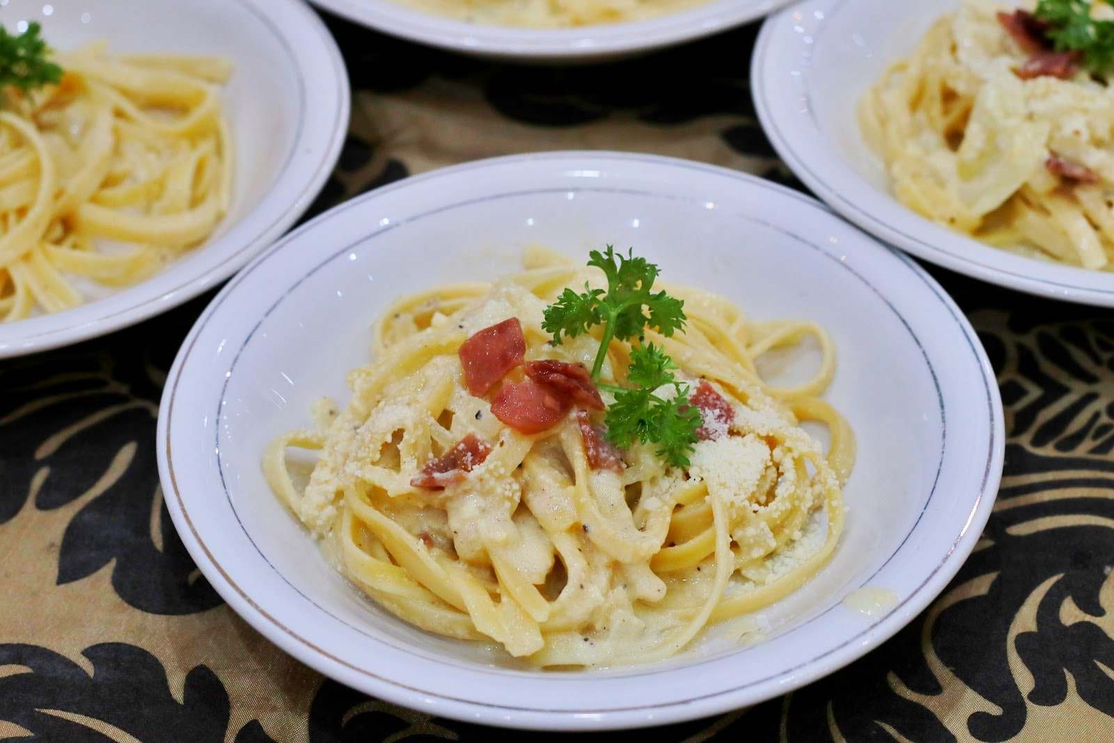 Pasta saus krim dengan taburan daging asap dan peterseli di piring saji