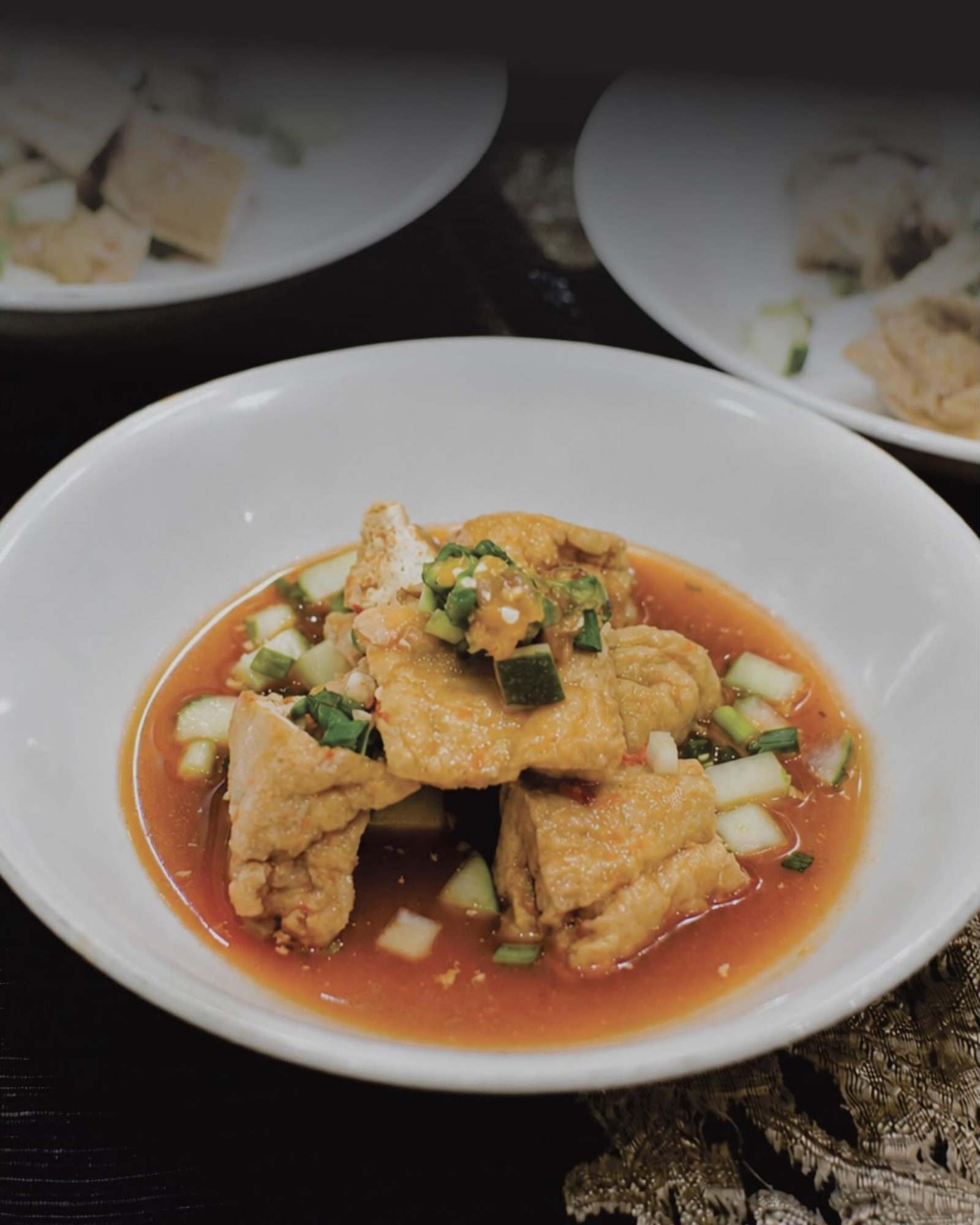 Tahu gejrot dengan kuah, irisan bawang, dan cabai di piring putih